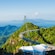 A curved pedestrian suspension bridge arcs across a lush mountain ridge above the Langkawi jungle